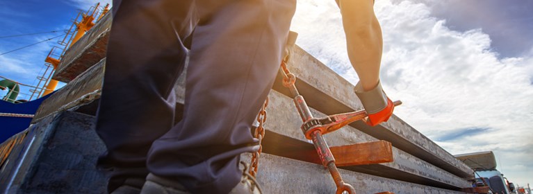 Man using ratchet lever binder to secure load on logging truck